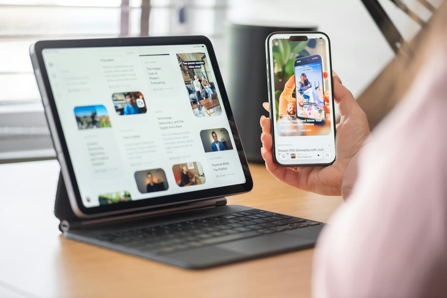 Hands holding a smartphone and tablet on a wooden desk.